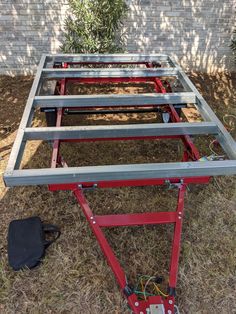 a metal frame sitting in the grass next to a brick wall with wires and tools on it