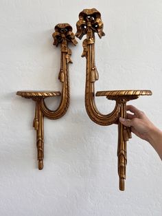 two golden wall sconces with flowers on them, one being held up by a person's hand