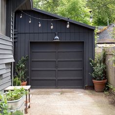 a garage with plants and lights hanging from it's side wall in front of a house