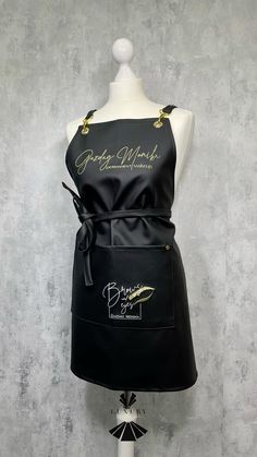 a mannequin wearing a black apron with gold trimmings and writing on it