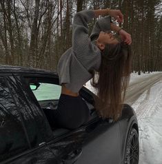 a woman leaning on the hood of a car in the snow with her hands behind her head