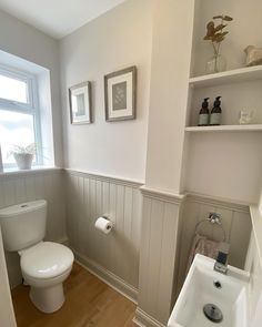 a white toilet sitting next to a sink in a bathroom under a window on top of a hard wood floor