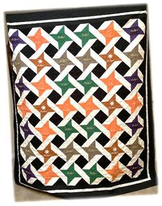 an orange, black and white quilt with stars on the top is hanging from a wall