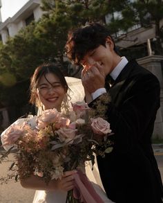 a bride and groom posing for a photo on the street with flowers in their hands