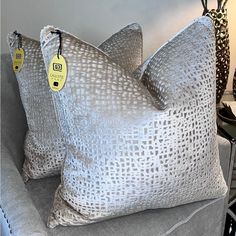 two pillows are sitting on a couch with tags attached to the back of one pillow