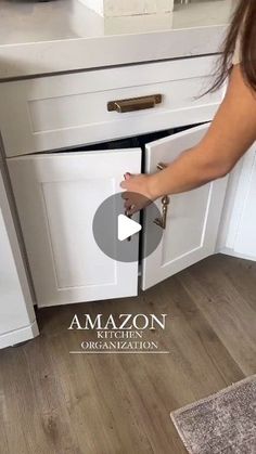 a woman is opening the door to an open kitchen cabinet in front of a sink