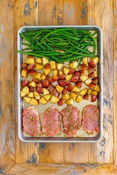 an overhead view of meat, potatoes and green beans on a baking sheet with a wooden background