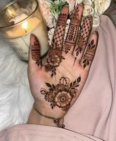 a woman's hand with henna on it next to a candle and flowers