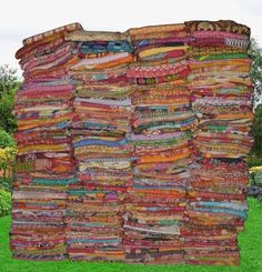 a large piece of cloth is stacked on top of each other in the grass with trees in the background