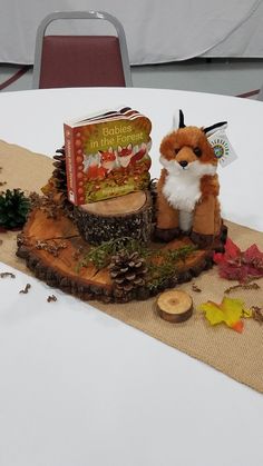 a stuffed fox sitting on top of a table next to a book and pine cones