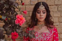 a woman wearing a red and gold outfit standing next to a brick wall with flowers