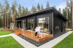 a man standing in front of a black house on a wooden deck surrounded by grass and trees