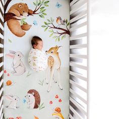 a baby is sleeping in his crib with woodland animals on the wall behind him