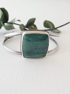 This large square Larsonite* is a deep sea-green color with darker greens sweeping across its surface. Simply set atop a cuff bracelet, the curving lines of silver give this statement cuff an elegant, feminine style. On the underside of the stone, waves of silver are cut away to reveal the beautiful underside of this u Modern Green Cuff Bracelet As Gift, Modern Green Cuff Bracelet Gift, Modern Green Cuff Bracelet For Gift, Modern Green Cuff Bangle Bracelet, Handmade Green Cuff Bracelet For Formal Occasions, Elegant Feminine Style, Sea Green Color, Green Jasper, Elegant Feminine