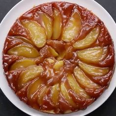 a white plate topped with a cake covered in caramel and apple slices on top of a black table