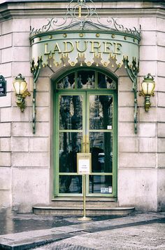 the front entrance to a building with green glass doors and gold trimmings on it