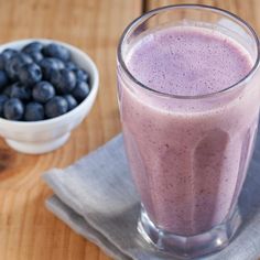 a smoothie in a glass next to a bowl of blueberries on a napkin