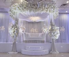 an elegant wedding setup with white flowers and chandeliers on the ceiling, along with couches