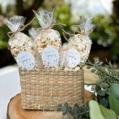 three bags of popcorn sitting on top of a wooden table next to greenery and flowers