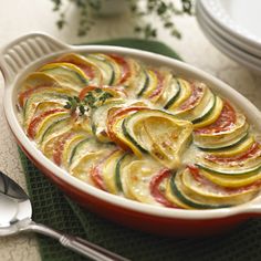 a casserole dish filled with vegetables on top of a green place mat next to silverware