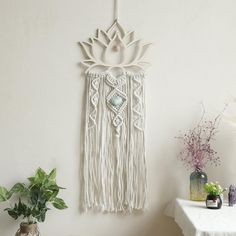 a white wall hanging next to a potted plant on top of a wooden table