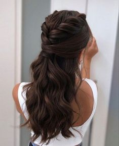 a woman with long brown hair wearing a half up braid hairstyle in front of a mirror