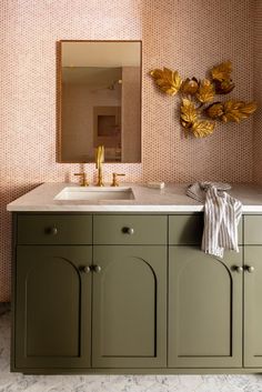 a bathroom with green cabinets and a gold mirror above the sink in front of it