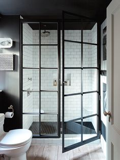 a white toilet sitting next to a shower in a bathroom under a window with glass doors