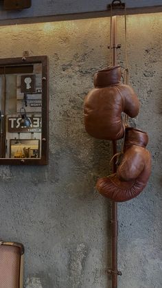 two brown leather boxing gloves hanging from the side of a wall next to a mirror