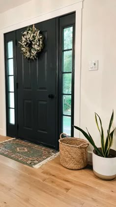 a black front door with a wreath and potted plant on the floor next to it