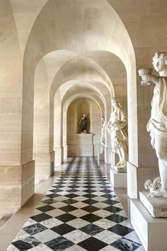 the hallway is lined with marble statues and checkerboard flooring in front of arches