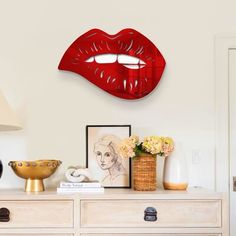 a white dresser topped with a vase filled with flowers next to a red wall mounted mirror