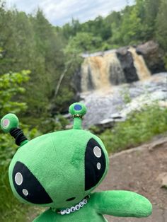 a green stuffed animal with a waterfall in the background