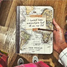 someone holding a pen and writing on a notebook with a world map in the background