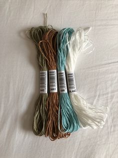 three skeins of yarn are laying on a white bed sheet, one is blue and the other is green