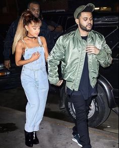 a man and woman walking down the street at night with one person wearing overalls