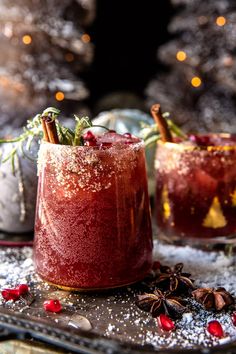 two glasses filled with red drink sitting on top of a metal tray next to a christmas tree