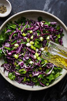 a white bowl filled with red cabbage and green onions next to a bottle of olive oil