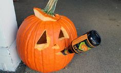 a carved pumpkin sitting next to a wall with a beer bottle in it's mouth