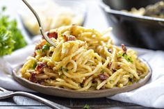 a fork full of pasta with bacon and parmesan cheese on the table next to other dishes