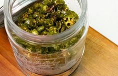 a jar filled with green peppers sitting on top of a wooden table next to a knife