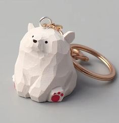 a white bear shaped keychain sitting on top of a gray table next to a gold ring