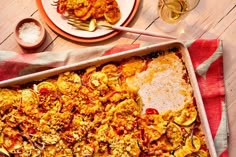 a casserole dish on a red and white tablecloth next to two plates with silverware