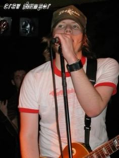 a young man singing into a microphone while holding a guitar in front of his face