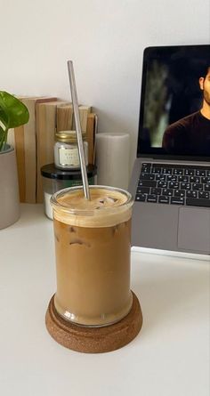 a laptop computer sitting on top of a desk next to a cup filled with liquid