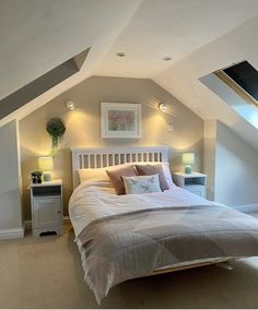 a bed sitting in the middle of a bedroom under a slanted ceiling with two lamps on either side of it