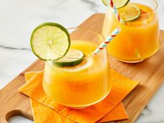 two glasses filled with orange juice on top of a wooden cutting board