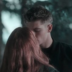 a young man and woman are kissing in the dark forest, with their eyes close to each other