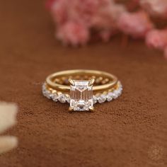 an engagement ring and wedding band set on a brown surface with flowers in the background