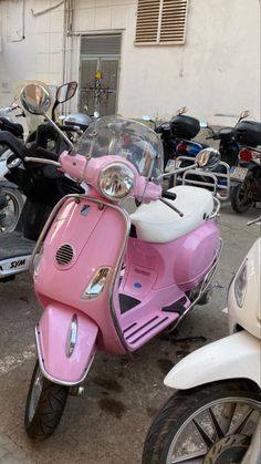 a pink scooter parked in front of a building next to other mopeds